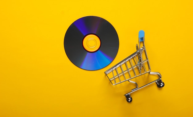 Carrito de la compra con disco cd sobre superficie amarilla