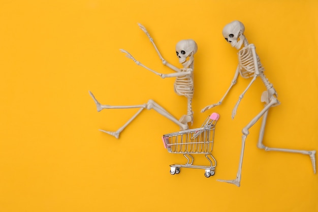 Foto carrito de la compra con divertidos esqueletos sobre fondo amarillo. tema de halloween. vista superior