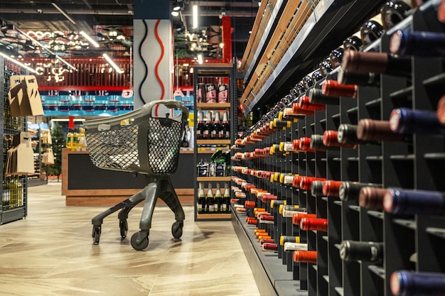 Carrito de compras abandonado cerca de estantes de vino en una tienda de comestibles