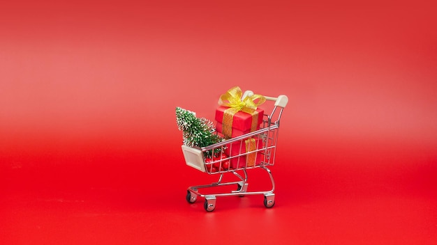 Carrito de compras con árbol de Navidad y regalos Concepto de compras y regalos de Año Nuevo y Navidad En un fondo rojo diseño minimalista