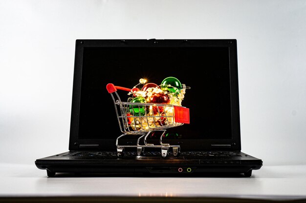 Carrito de compras con bolas de navidad y guirnaldas en el teclado de la computadora portátil