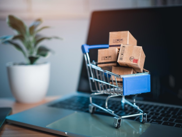 Foto el carrito de compras y las cajas de productos colocadas en la computadora portátil representan el concepto de compras en línea