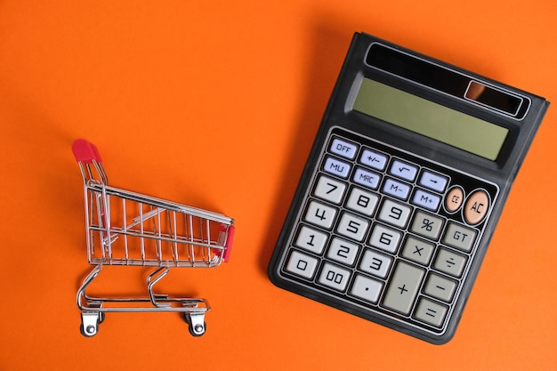 Carrito de compras y calculadora sobre fondo naranja presupuesto familiar y compras