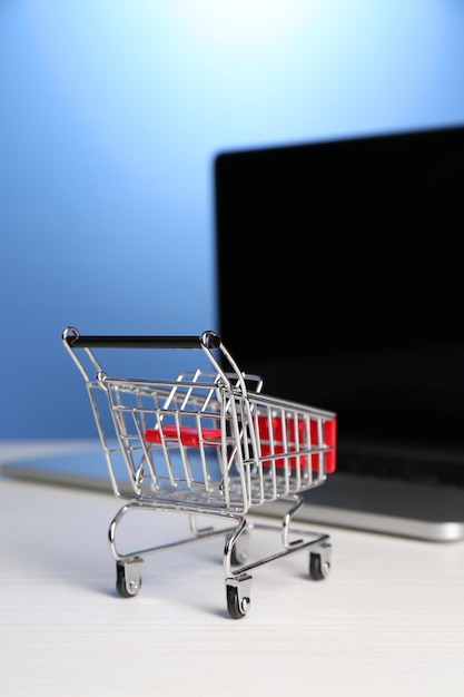 Carrito de compras en la computadora portátil sobre la mesa sobre fondo azul