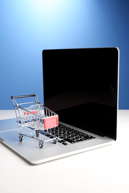 Carrito de compras en la computadora portátil sobre la mesa sobre fondo azul
