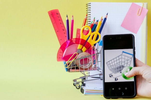 Foto carrito de compras con diferentes artículos de papelería en el fondo amarillo