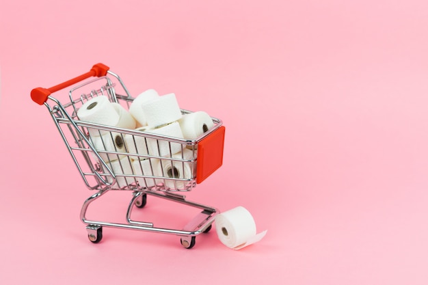 Un carrito de compras lleno de papel higiénico sobre un fondo rosa. Concepto COVID-19. Copia espacio