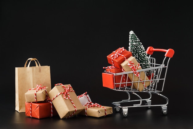 Carrito de compras lleno de varias cajas de regalo y un árbol de Navidad en negro