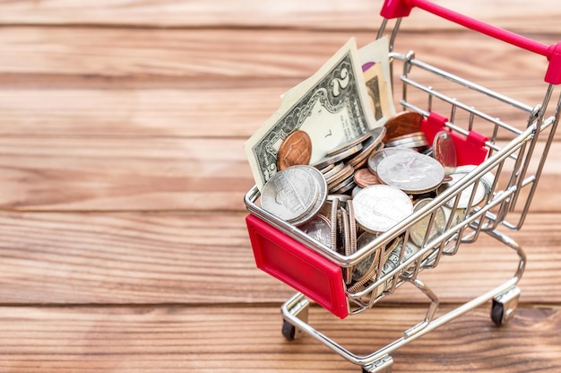 Carrito de compras con monedas y billetes de dólar en fondo de madera Espacio para texto Encerrar concepto de negocio