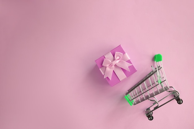 Carrito de compras y papel de regalo con lazo en superficie rosa claro