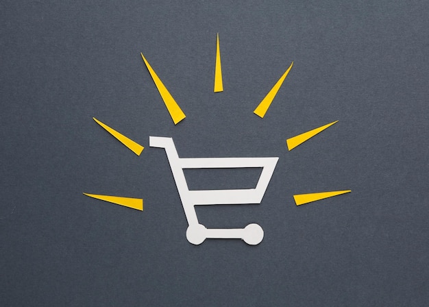 Carrito de compras con rayos de luz cortados de papel sobre un fondo gris