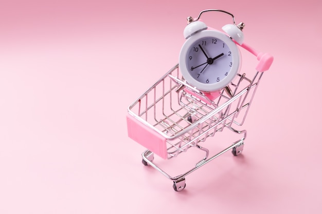 Foto carrito de compras y reloj despertador blanco sobre rosa