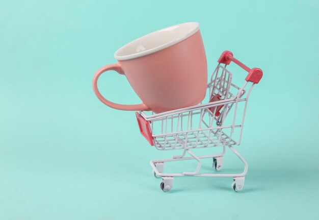 Foto carrito de compras con taza de cerámica sobre fondo azul