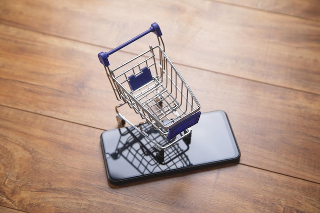 Carrito de compras con un teléfono inteligente en la mesa de madera