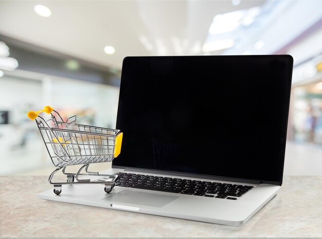 Carrito de compras a través de un portátil aislado en segundo plano.