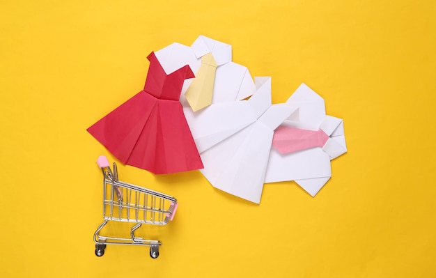 Carrito de compras con vestidos y camisas de Origami con corbata sobre fondo amarillo