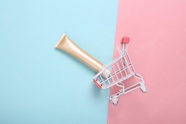 Carrito de supermercado con tubo de fundación en fondo pastel rosa azul