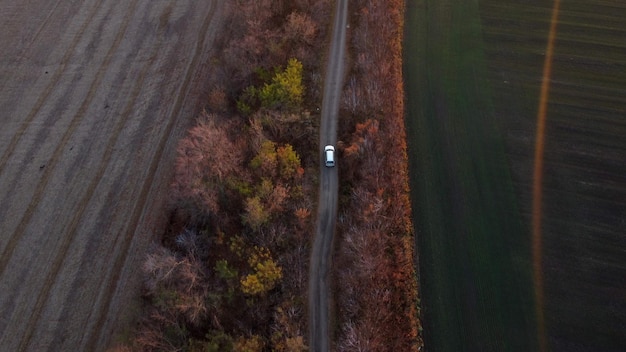 Carro branco dirigindo estrada de terra entre campos agrícolas campo outono noite vista aérea d