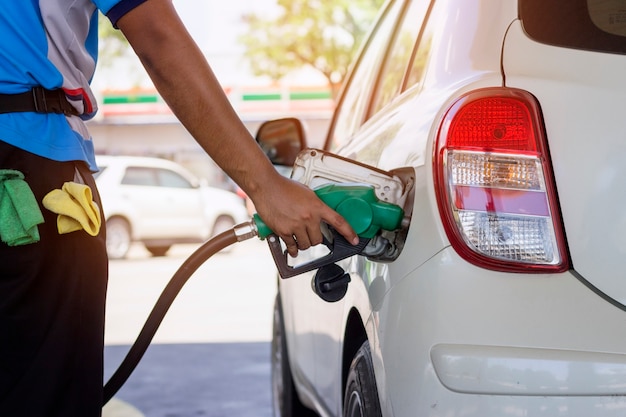 Carro branco reabastecimento de gasolina pelo bocal do distribuidor automático no posto de gasolina com a luz solar quente