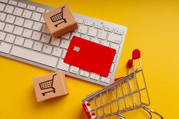 Carro de cajas de tarjetas y tarjeta de crédito roja en un teclado sobre un fondo amarillo Primer plano