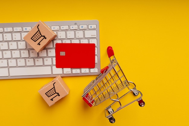 Carro de cajas de tarjetas y tarjeta de crédito roja en un teclado sobre un fondo amarillo Vista superior