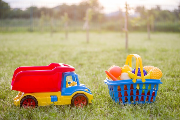Foto carro camión y una canasta con frutas y verduras de juguete. juguetes de plástico de colores brillantes para niños al aire libre en un día soleado de verano.