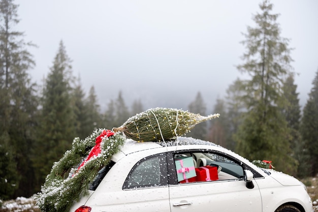 Carro com guirlanda de árvore de natal e presentes dentro na estrada de montanha