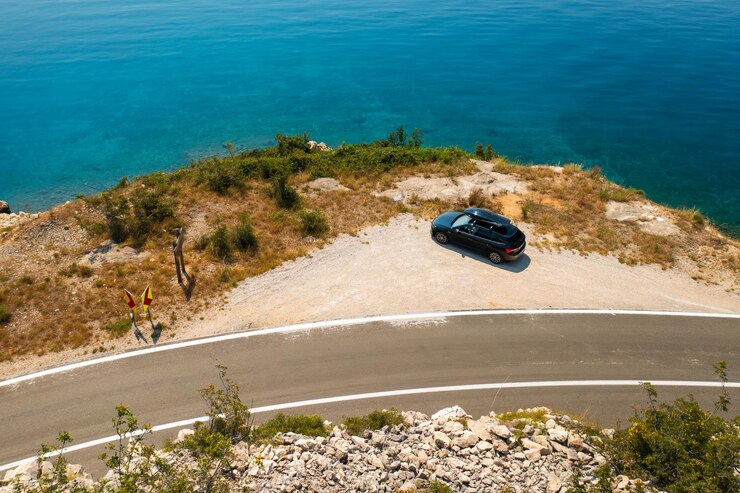 Foto carro com uma caixa de telhado estacionado perto de uma estrada acidentada com o mar azul abaixo cercado por escarpados