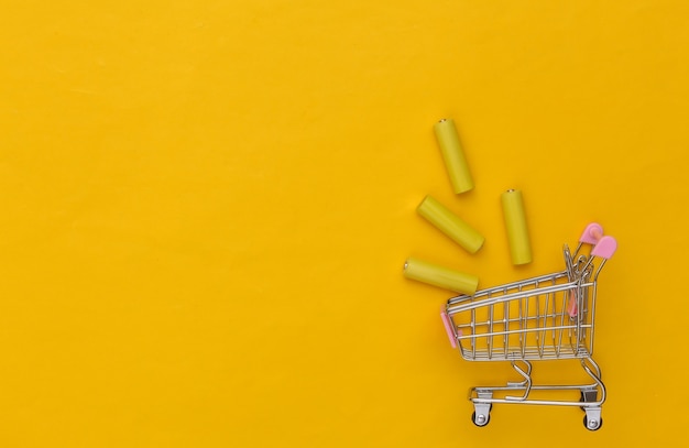 Carro de la compra con cuatro pilas AA de color amarillo sobre fondo amarillo. Vista superior