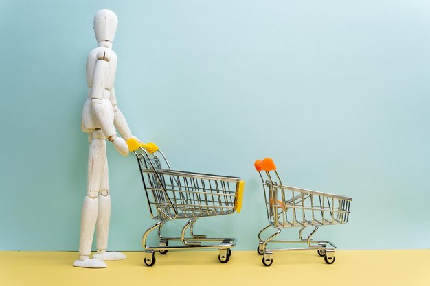 Carro de compras con bolsas de compras de maniquí de hombre de madera sobre fondo azul Idea creativa para el concepto de supermercado de compras en línea Espacio de copia