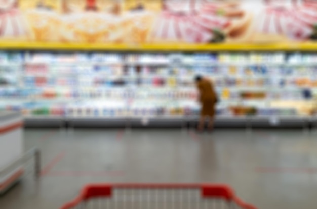 Carro de compras en borrosa de productos de consumo en estantes iluminados en el supermercado