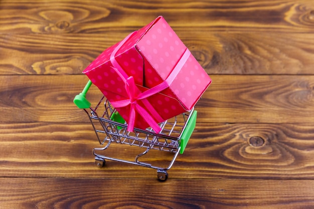 Carro de compras con caja de regalo grande sobre fondo de madera