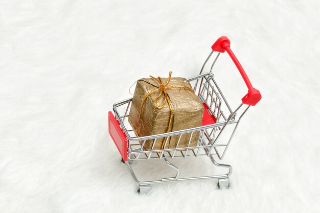 Carro de compras con caja de regalo sobre fondo blanco.