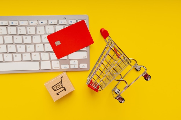 Carro de compras con caja y tarjeta de crédito roja en un teclado Compras y entregas en línea