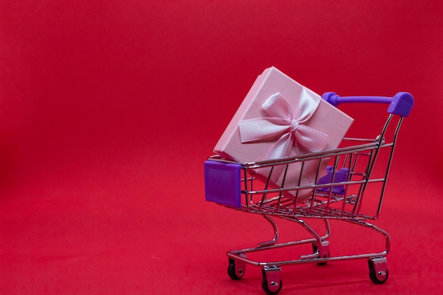 Carro de compras con cajas de regalos en un fondo rojo, lugar para texto.