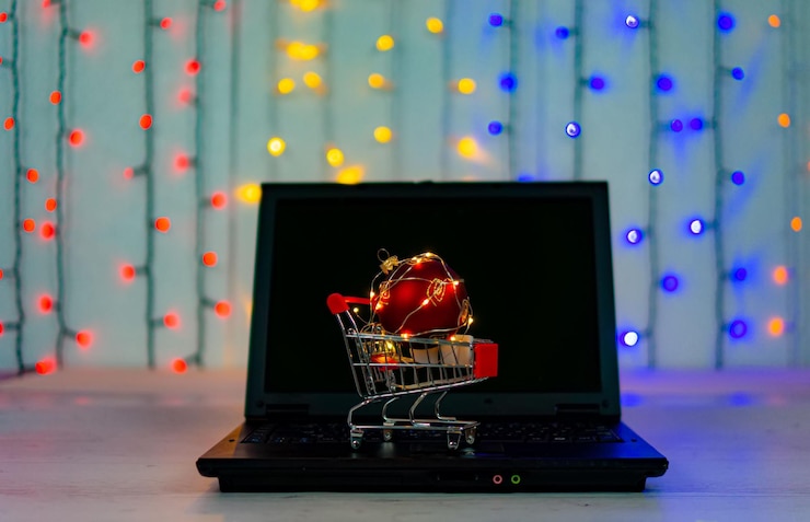 Foto carro de compras con gran bola de navidad y guirnaldas en el teclado de la computadora portátil