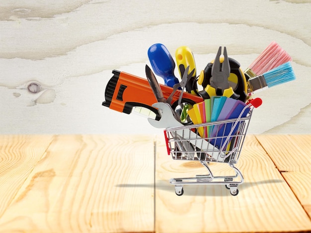 Carro de compras lleno de herramientas de construcción, aislado sobre fondo de madera