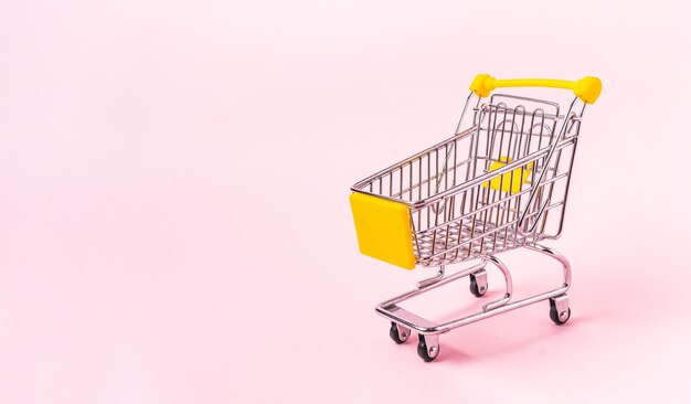 Carro de compras en miniatura aislado sobre un fondo rosa con espacio para copiar