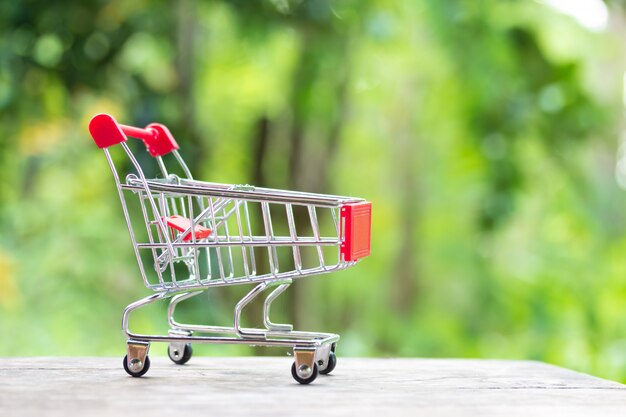 Carro de compras en miniatura en maqueta de madera sobre jardín verde borroso en la luz del mediodía