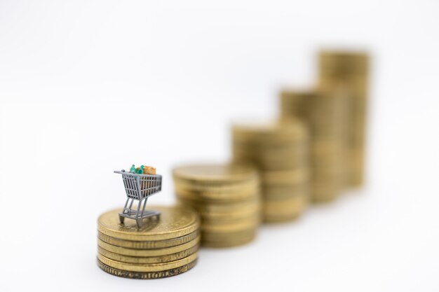 Carro de compras en miniatura o trolley en la parte superior de la pila de monedas de oro usadas en blanco