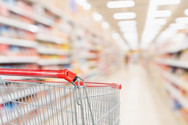 Carro de compras vacío con pasillo de tienda de descuento de supermercado de desenfoque abstracto y estantes de productos