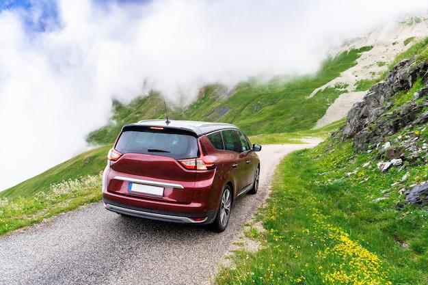 Carro da família de porta traseira vermelho escuro na estrada serpantina no alto das montanhas na frança em tempo chuvoso. viagem em família nos alpes. nuvens cercam o automóvel.