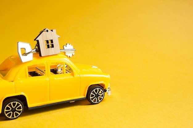 Carro de brinquedo amarelo com uma chave da casa no telhado em um fundo de cor. Mudança para uma nova casa, hipoteca, compra de um apartamento, táxi. Copie o espaço.