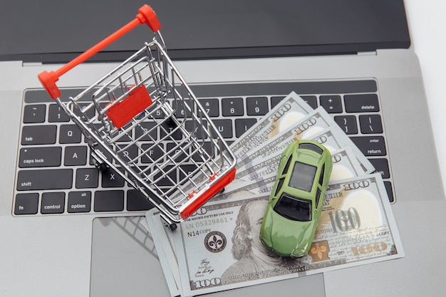 Carro de brinquedo e carrinho de compras com dinheiro em um laptop. Conceito de carro de compra online.