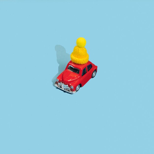 Carro de brinquedo vermelho com tampa de inverno amarela sobre fundo azul