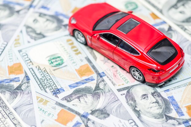 Foto carro de brinquedo vermelho está de pé em notas de dólar custo de compra de combustível de carro