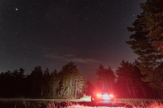 Carro de cena noturna com faróis na visão traseira em uma floresta sob um céu estrelado no outono foto com pouca luz Foto de alta qualidade