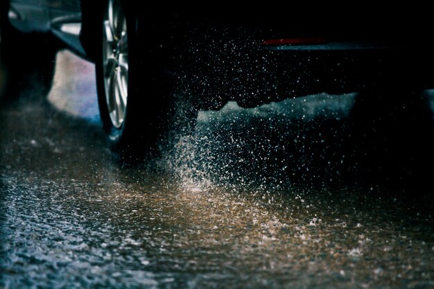 Carro de movimento na grande poça de chuva com água salpicando das rodas