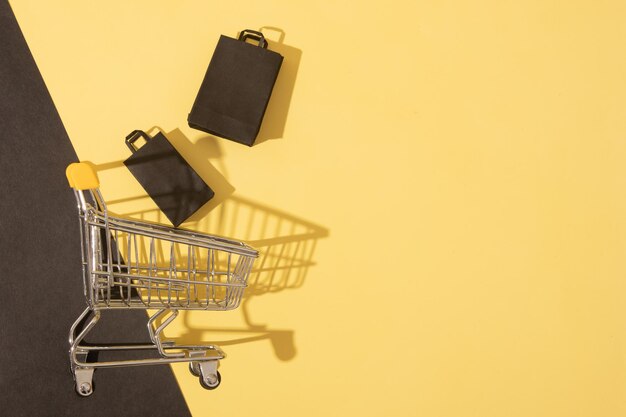 Carro de supermercado em miniatura plano com sacos de compras em venda de sexta-feira preta em fundo amarelo