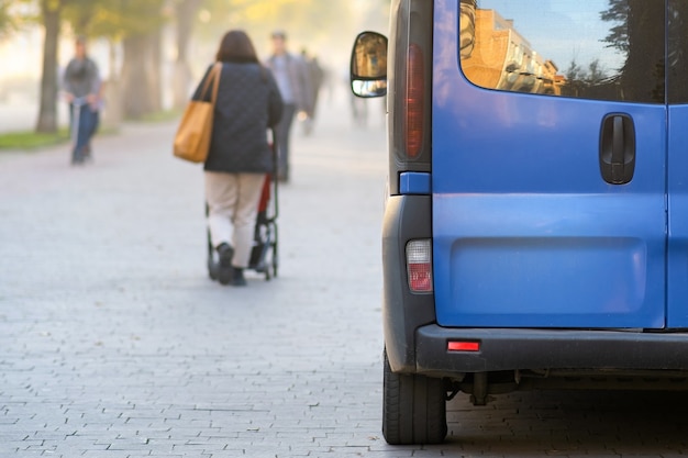 Carro de van de passageiros estacionado em um beco da cidade ao lado de uma rua com turva pedestres andando no outono.